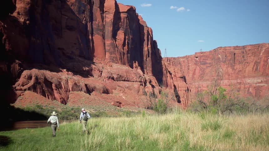 Two men are walking towards a river that runs next to a canyon wall
