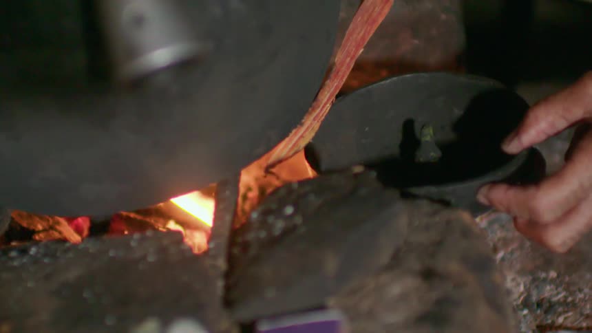 Someone is placing a pan next to a fire