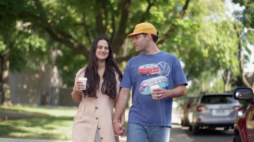 A man and woman hold hands and talk while walking in a neighborhood in daylight