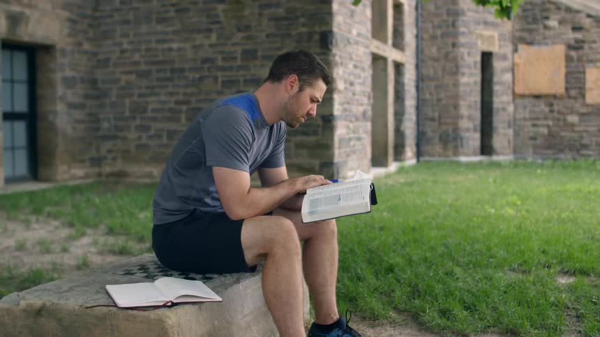 A man reads a book outside a building