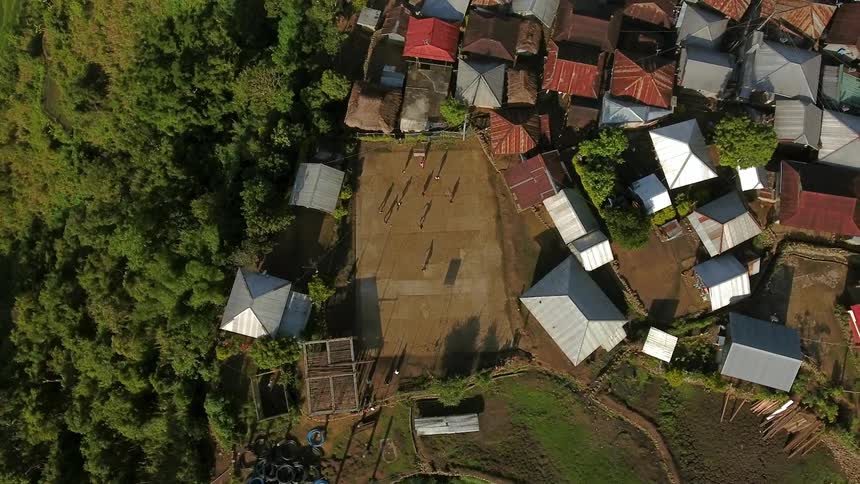 People are running around a soccer field in the middle of a small village