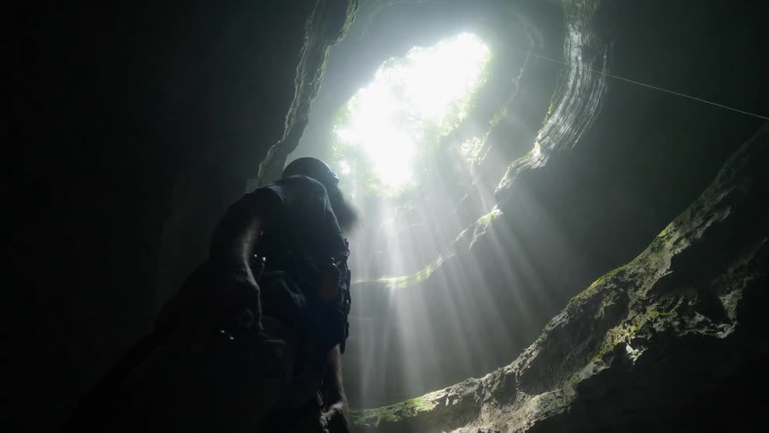 Someone is standing in a cave with a hole in the roof and they are looking up through it
