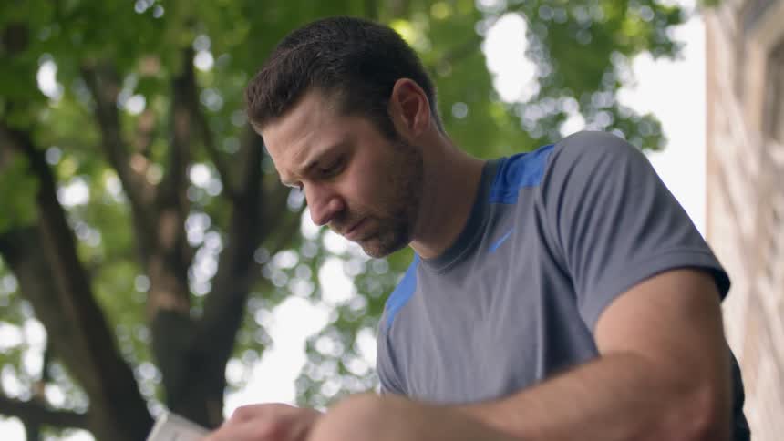 A man looks down at his phone under a tree