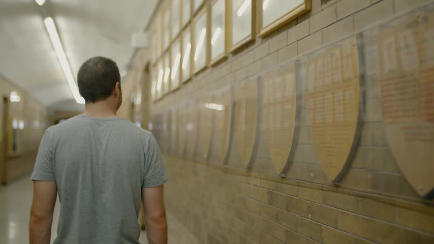 Man looks at plaques hanging on wall in hallway