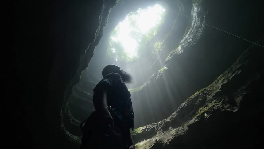A man looks up from the bottom of a cavern