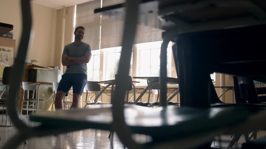A man leans against a desk in a classroom