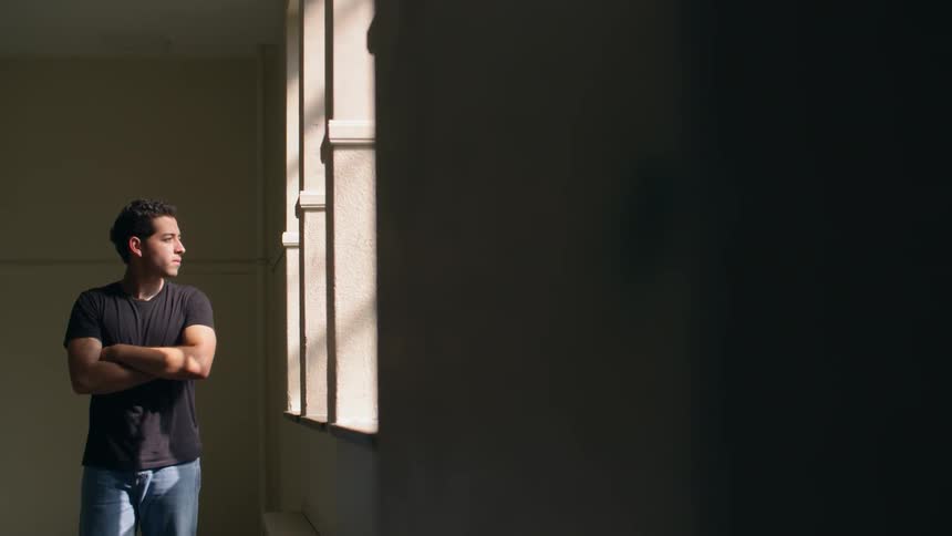 A man looks out of a window with arms crossed