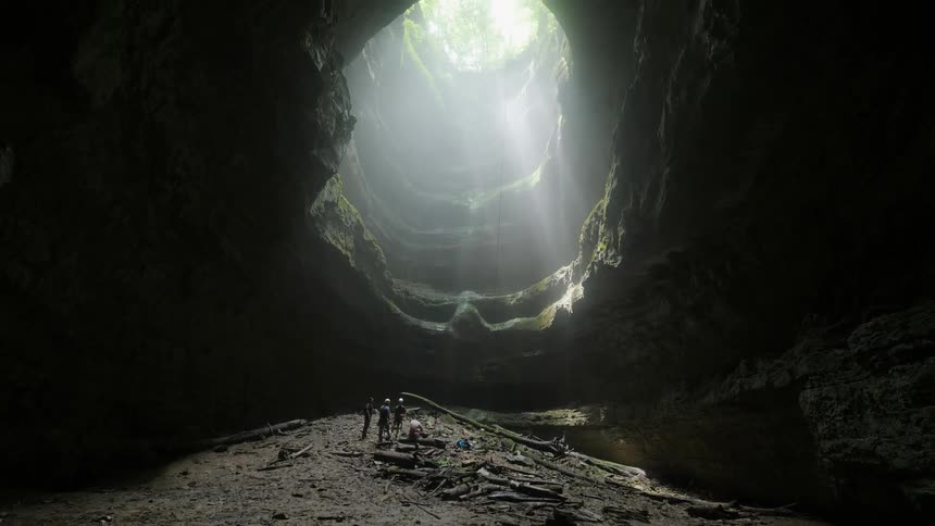 Three people stand and look up out of a deep cavern