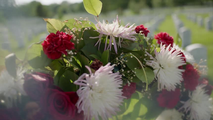 A bouquet of flowers rests on a headstone at a cemetery during the day