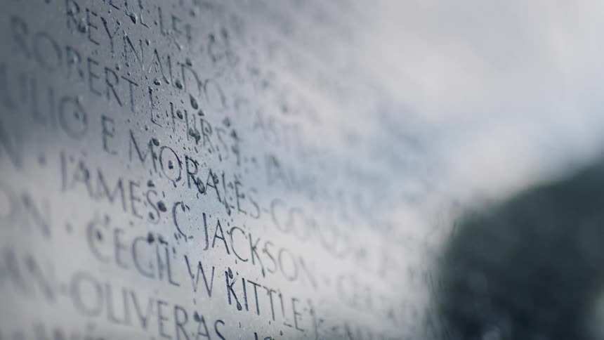 Dew hangs over names etched into a memorial wall