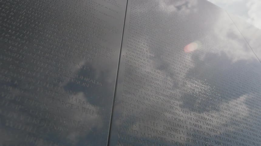 A granite wall etched with names is reflecting a cloudy sky