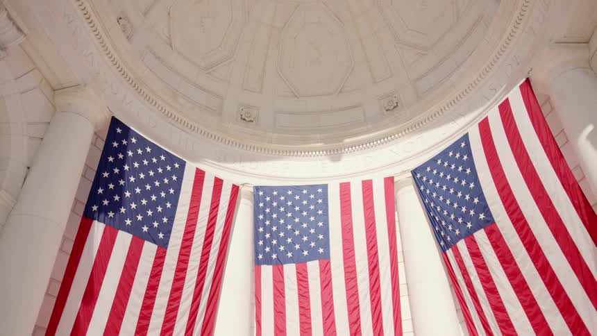 Us flags are hanging in the sunshine beneath a domed ceiling