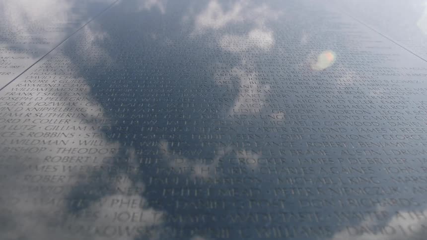 A war memorial etched with many names is reflecting a cloudy sky during the day