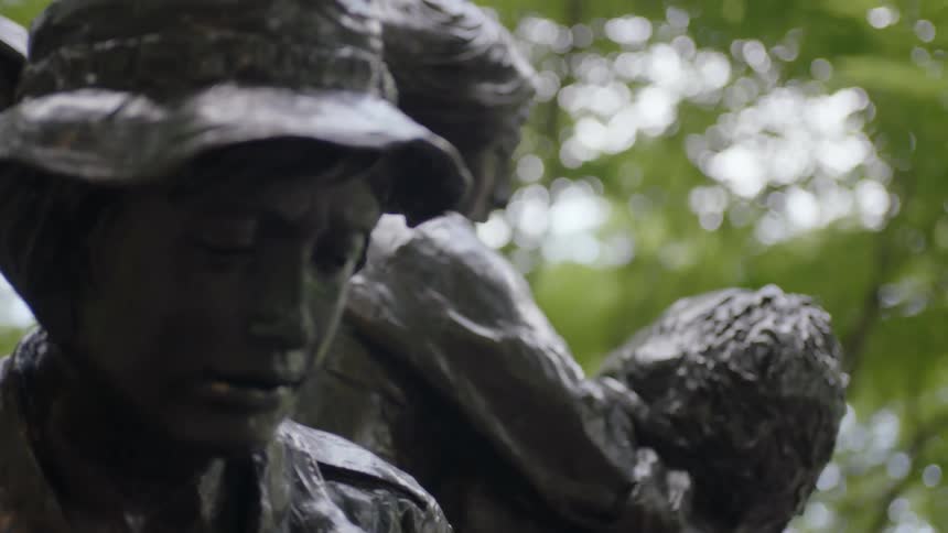 A statue of a woman in a hat is displayed under trees