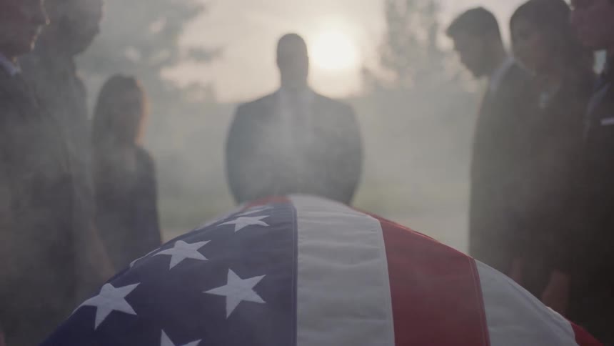 An american flag is wrapped over a casket at a funeral