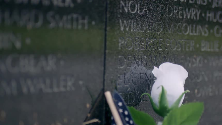 Flowers and a small flag rest against a memorial with names
