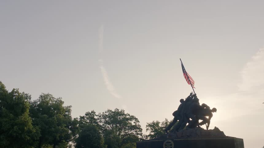 An american flag waves in a breeze at a war memorial statue