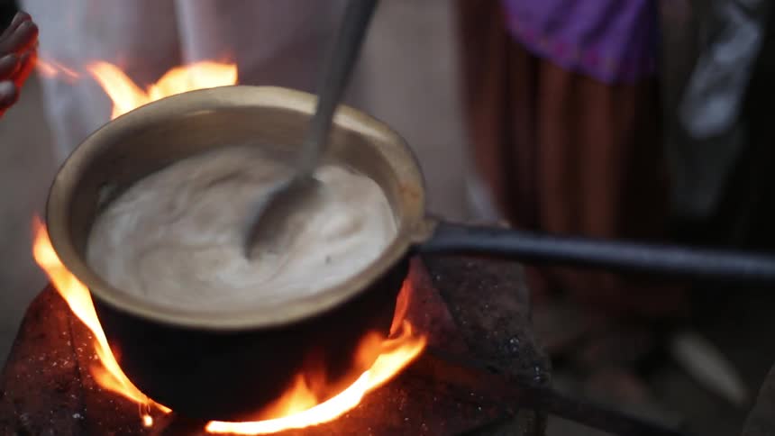 A pot is stirred over an open flame