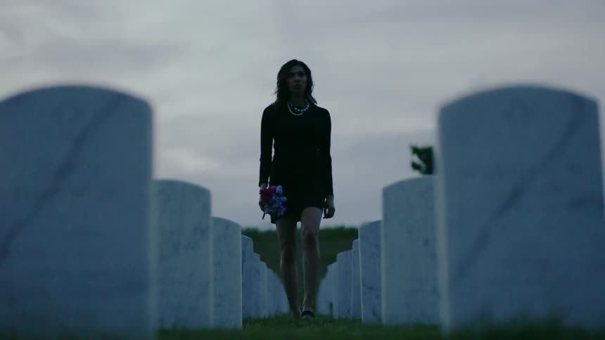 A woman in black holding flowers walks through a row of gravestones