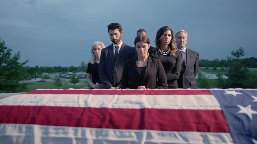 People grieve by a flag draped casket