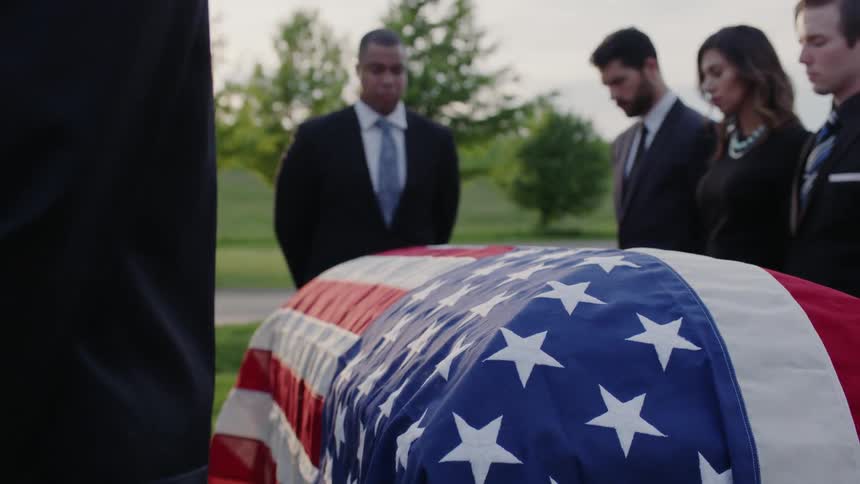 Men and women mourn in silence over flag draped casket at funeral