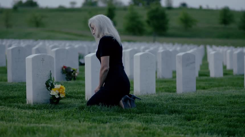 A woman grieves in front of a headstone