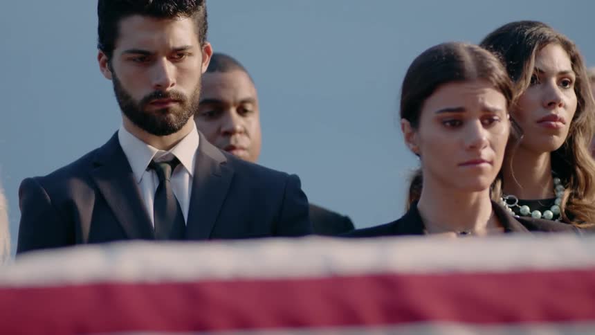 A ground of people are sad as they look at an american flag covered coffin