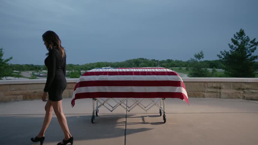A line of people are walking past an american flag covered coffin
