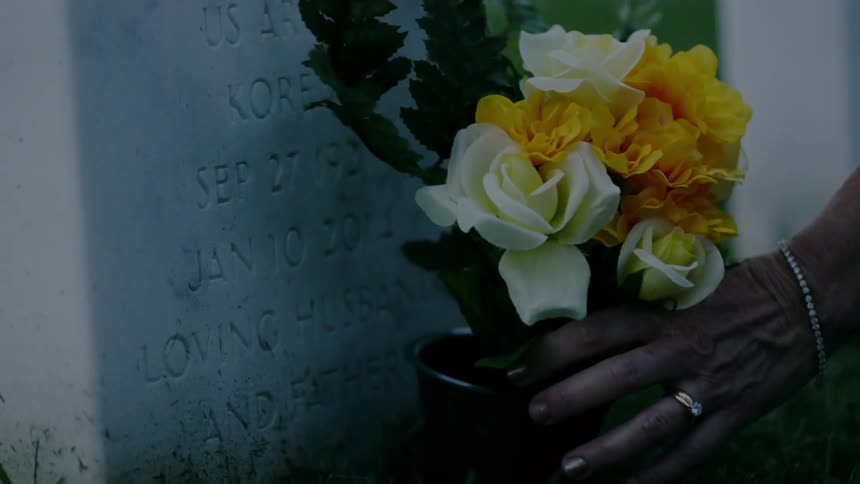 A woman places flowers at a headstone