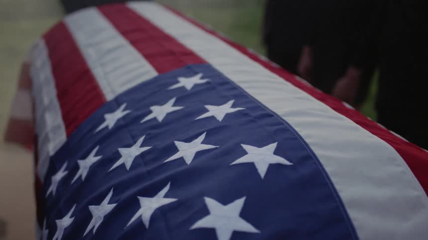 An american flag is wrapped over a casket at a funeral