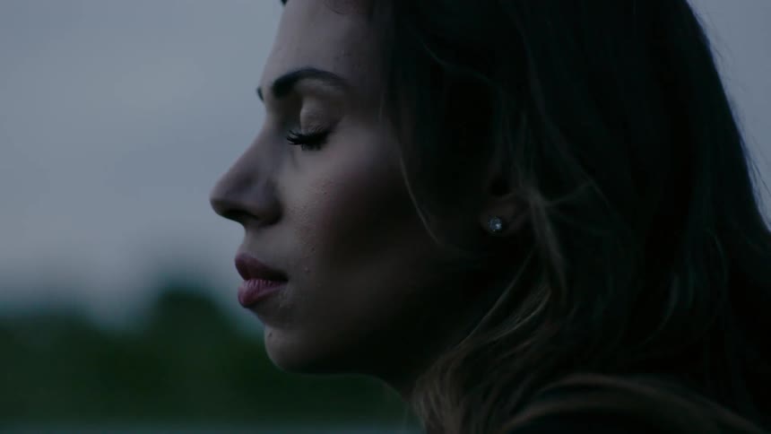 A woman is standing outside with her eyes close at dusk