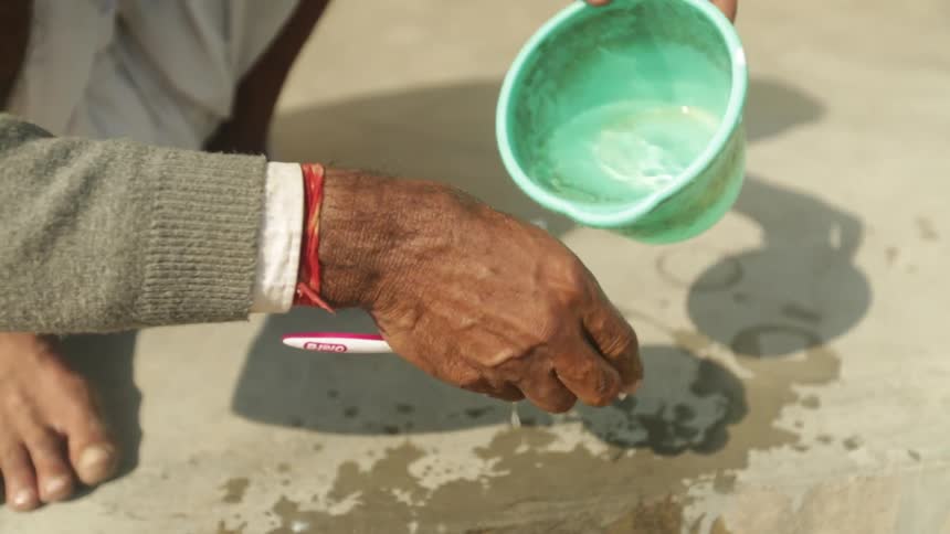 Someone pouring water from a cup to rinse a toothbrush