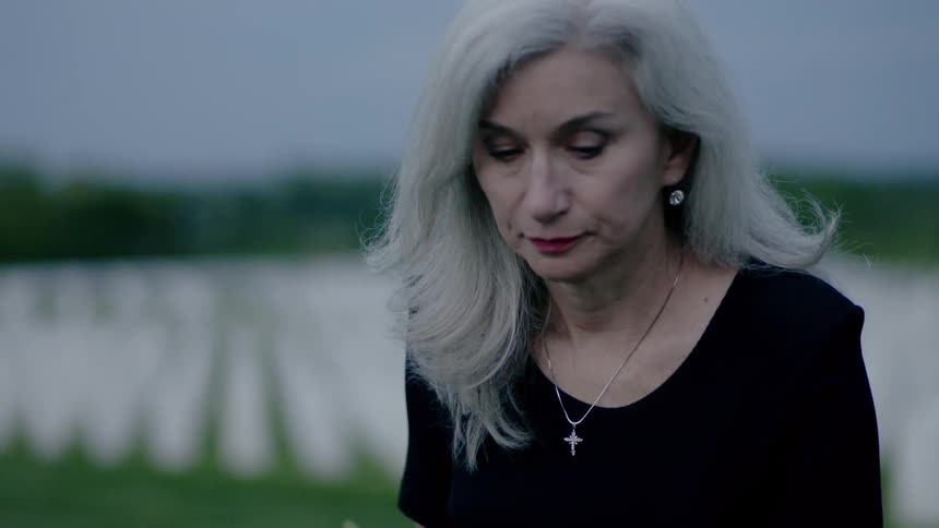 A woman kneels and places flowers on a grave