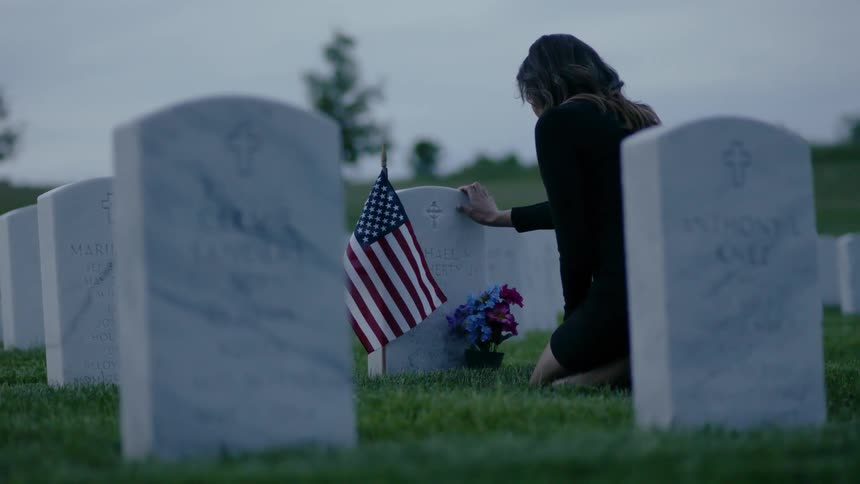 Woman kneeling in cemetery rests her hand on gravestone
