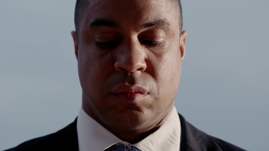 A black man in a suit is looking down and very sad