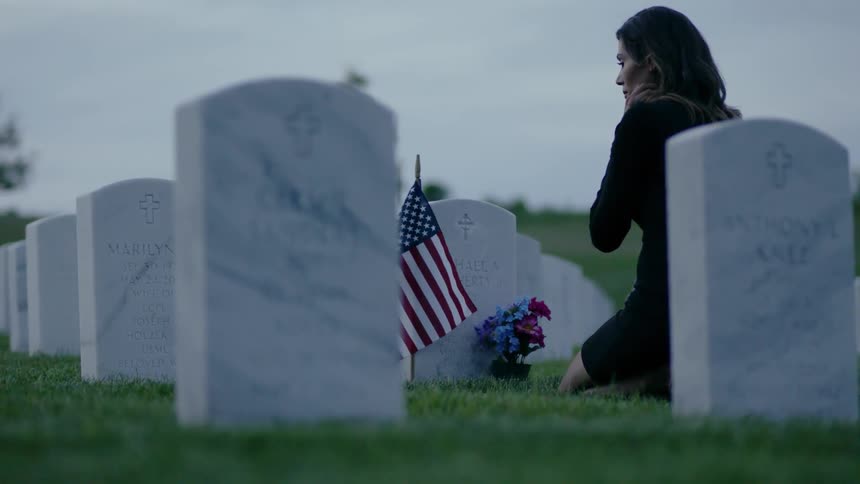 A woman is sitting on the grass in front of a soldiers grave
