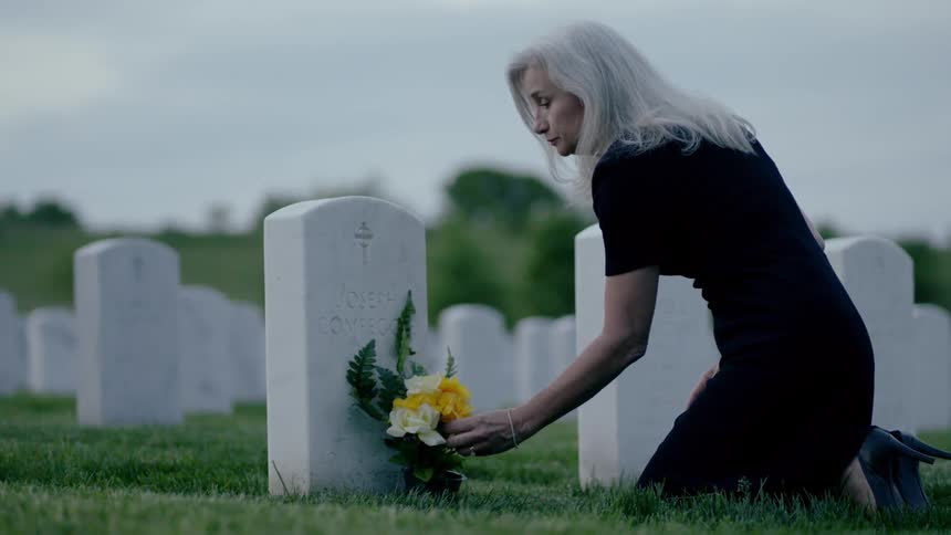 A woman places flowers at a grave