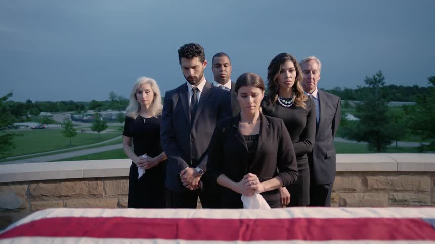 A family stands and looks at a flag draped coffin