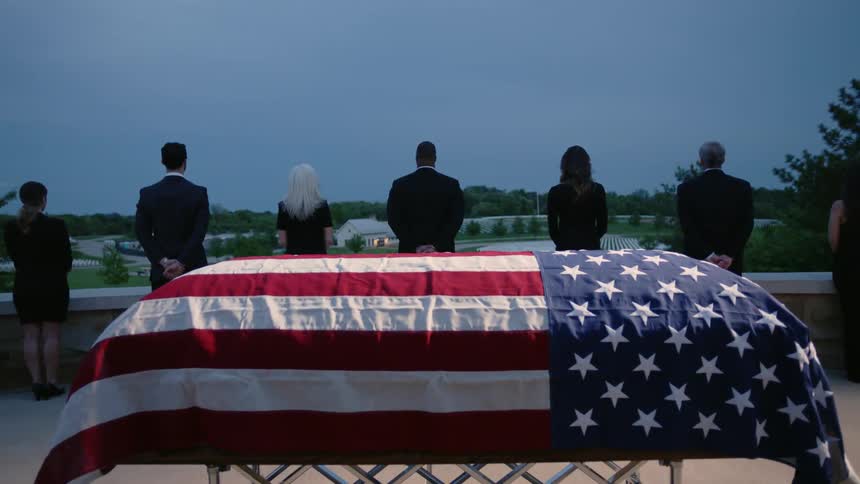 People grieve by a flag draped casket