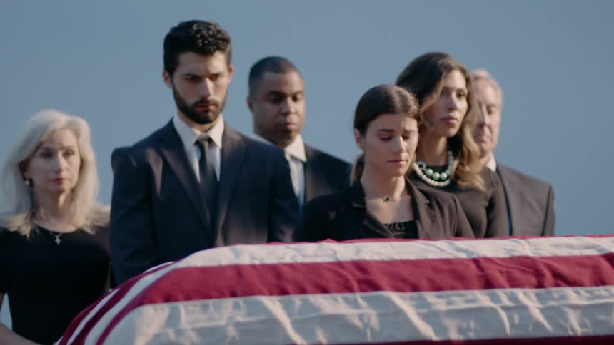 A group of people are standing around a flag covered casket