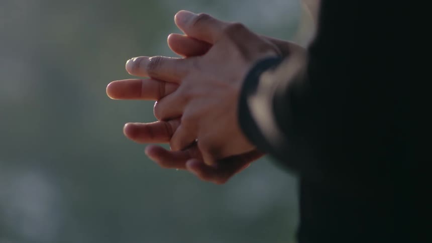 A man wearing a suit coat clasps his hands together