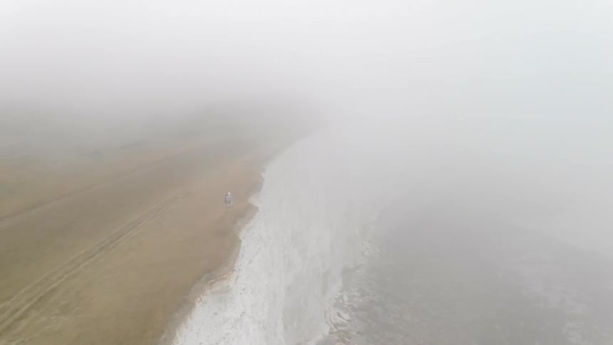 People are walking along a foggy cliff side