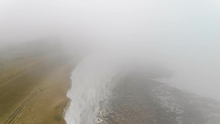 Fog hangs above a tall cliff by the water