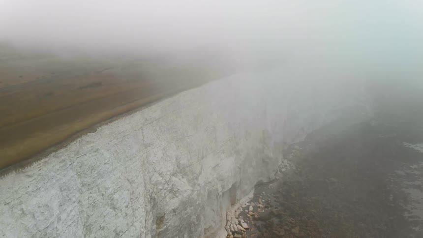 A fog covered cliff leads down to the ocean