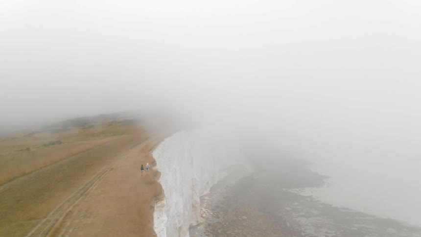People are standing on the ledge of a foggy cliff