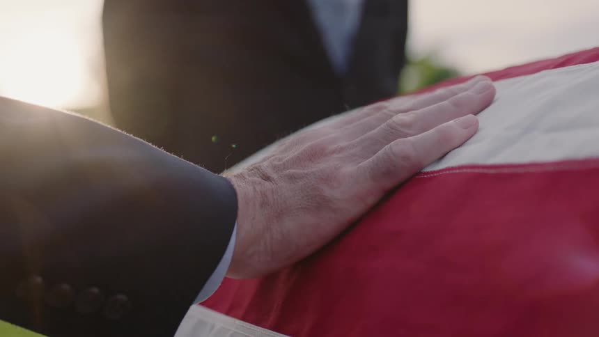 A person touches a coffin draped with a flag