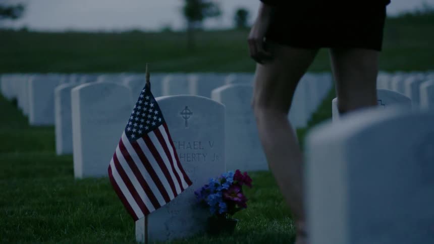 A woman is kneels before a soldiers grave