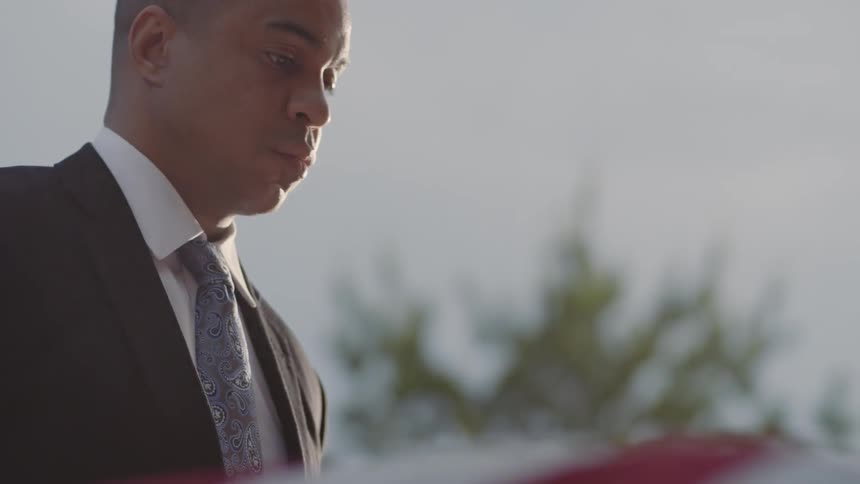 A man in suit and tie looks down at american flag on casket