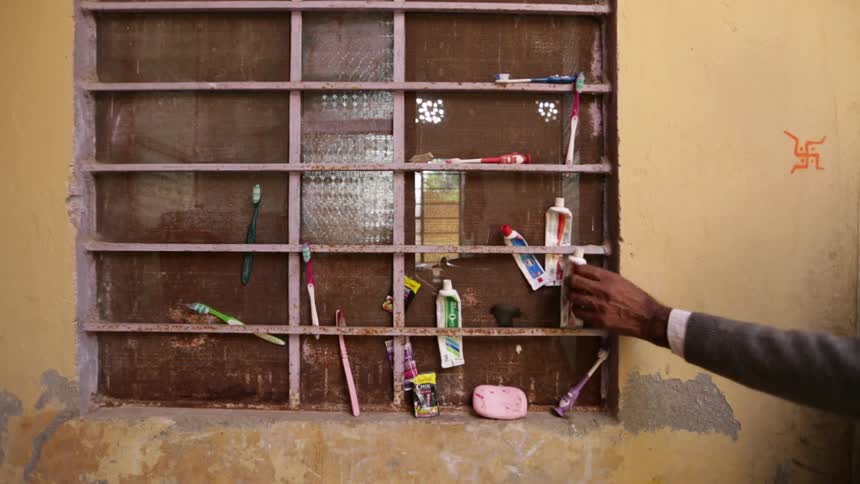 Someone takes a tube of toothpaste from a makeshift cupboard holding toothpaste and toothbrushes