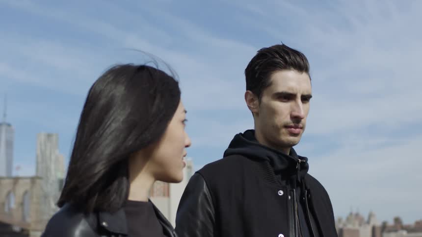 A man and woman walk outside with a city skyline behind them